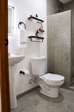 A bathroom with a toilet, sink, and shower. There are towel racks and a soap dispenser on the wall.