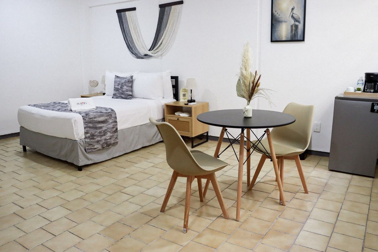 A hotel room with a bed, bedside table, lamp, and a small dining table with chairs.
