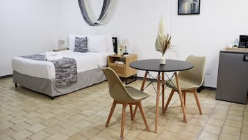 A hotel room with a bed, bedside table, lamp, and a small dining table with chairs.
