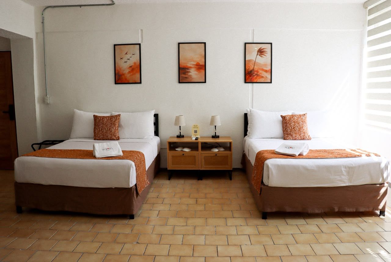 Habitación de hotel con dos camas, una mesita de noche y una obra de arte en la pared.
