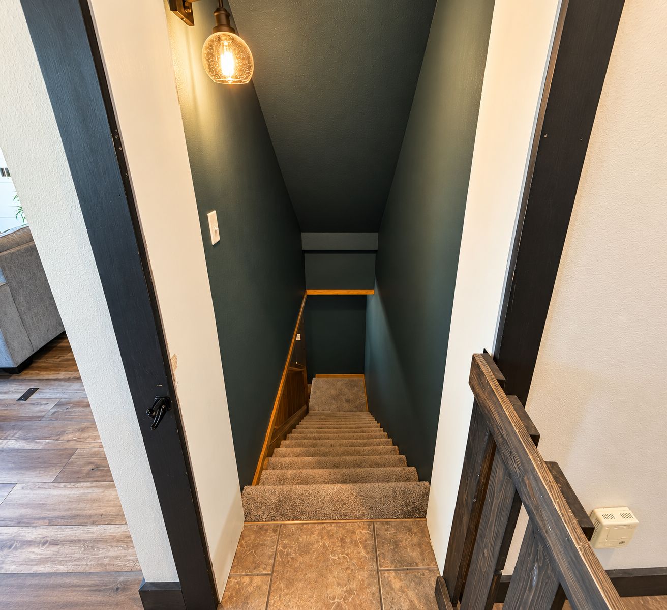 A staircase with a wooden handrail, carpeted steps, and a wall-mounted light fixture.