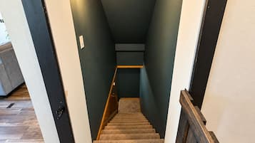 A staircase with a wooden handrail, carpeted steps, and a wall-mounted light fixture.