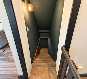Una escalera con barandilla de madera, peldaños alfombrados y un aplique en la pared.
