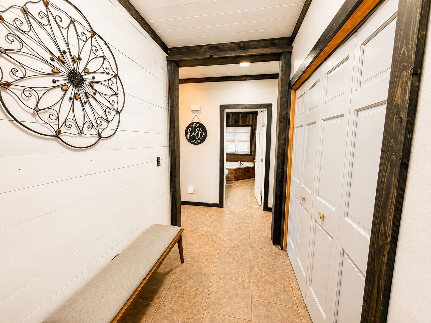 A hallway with a bench, a decorative metal wall piece, and a 'hello' sign.