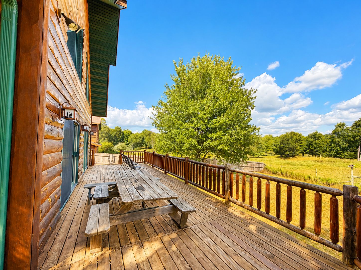 Um deck de madeira com mesas de piquenique e vista para um campo verde.