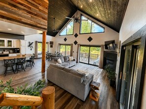 A spacious living area with a large sofa, a dining table, and a kitchen area with cabinets and a countertop. - NEW ATV Trail | Fire Pit | Deck | Trailer Parking (Birchwood)