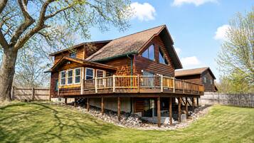 Eine zweistöckige Blockhütte mit einem Balkon, umgeben von einer Holzterrasse und einem Steinfundament.