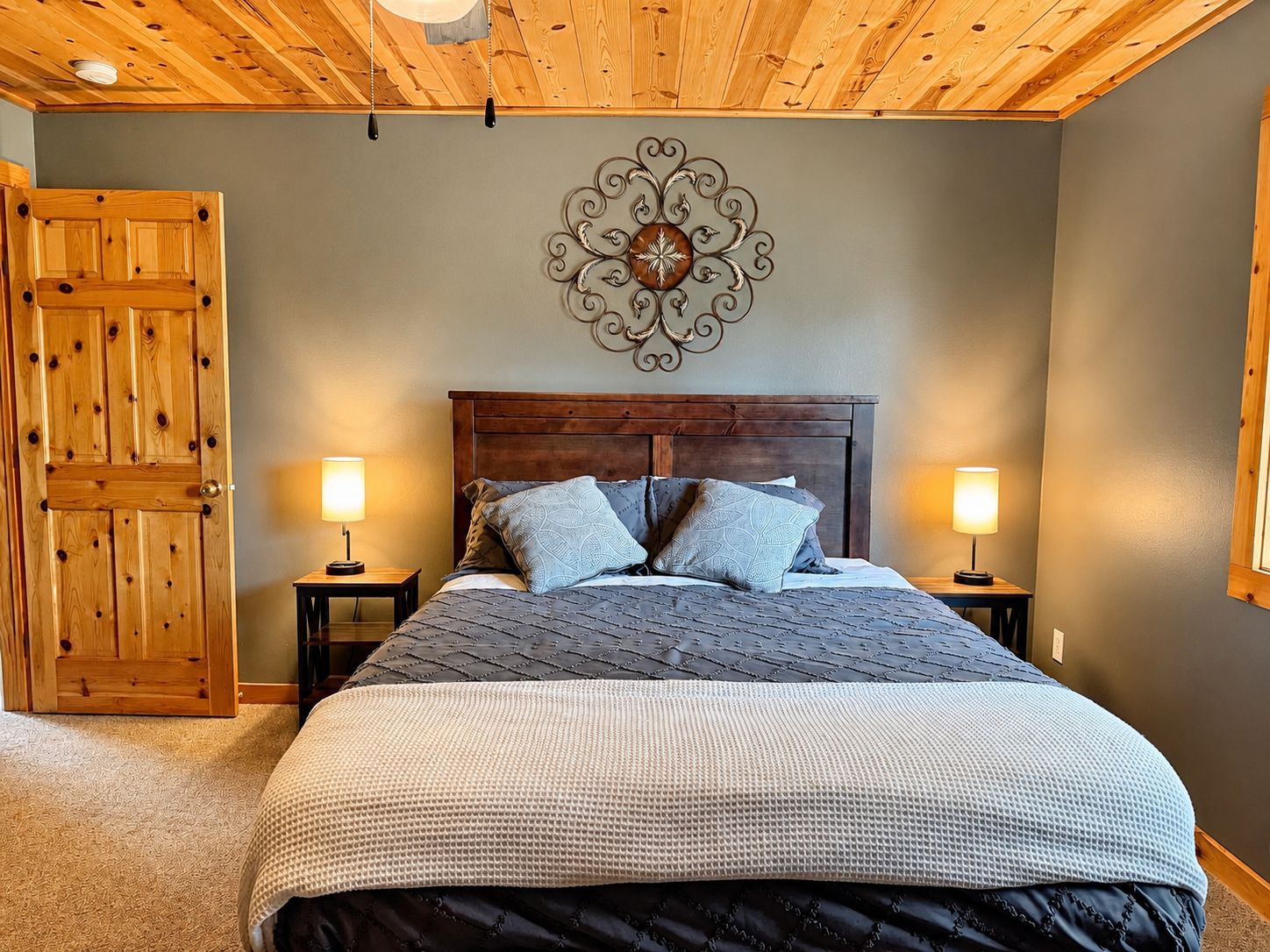 Ein Schlafzimmer mit Holzbalkendecke, einem Bett mit gesteppter Bettdecke, zwei Nachttischlampen und einem dekorativen Wandbild.