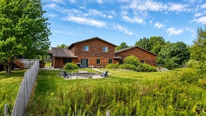 A wooden cabin with a patio area, surrounded by lush greenery and a clear sky.