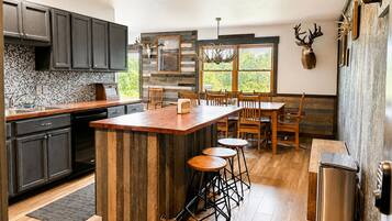 Una cocina moderna con armarios oscuros, una isla de madera y un comedor con vistas a zonas verdes.