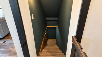 Una escalera con barandilla de madera, peldaños alfombrados y un aplique en la pared.