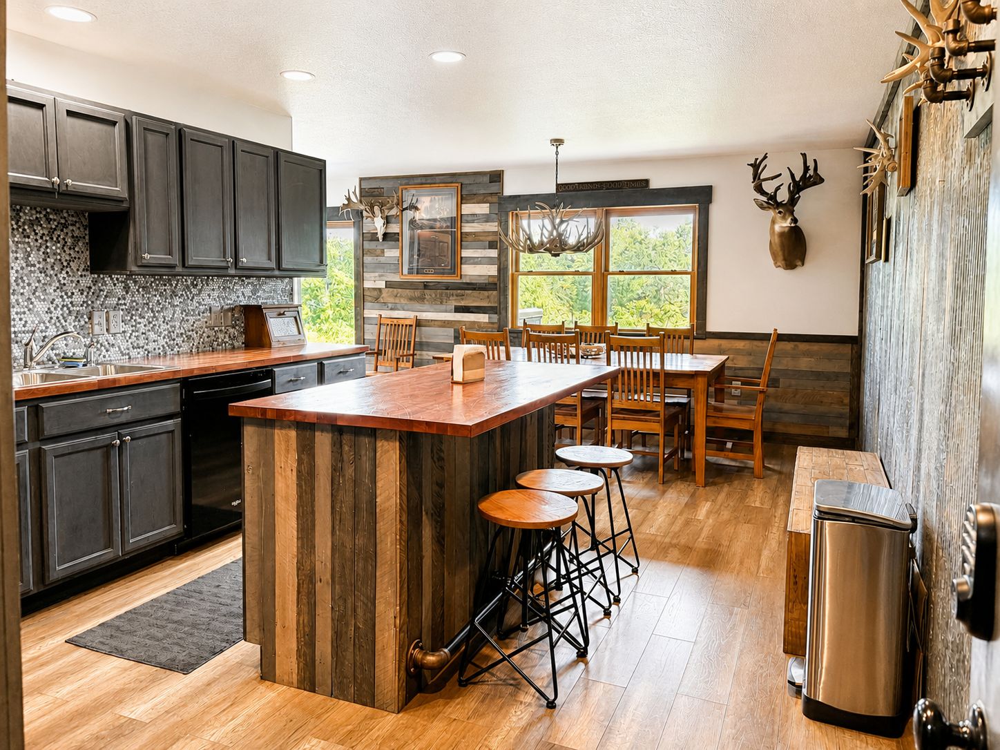 A modern kitchen with dark cabinets, a wooden island, and a dining area with a view of greenery.