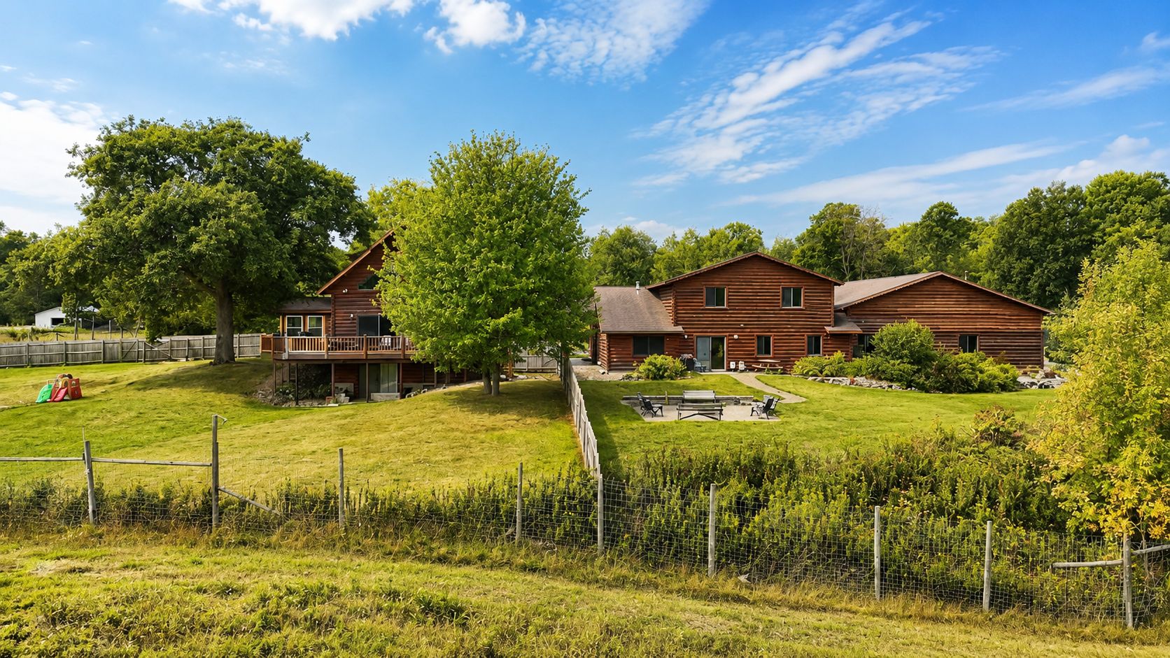 Eine Holzhütte mit einer Terrasse, umgeben von einem eingezäunten Garten und üppigem Grün.