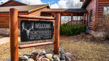 Cartell de benvinguda per a Northwoods Antler Lodge, amb una estructura de fusta rústica i fonaments de pedra.
