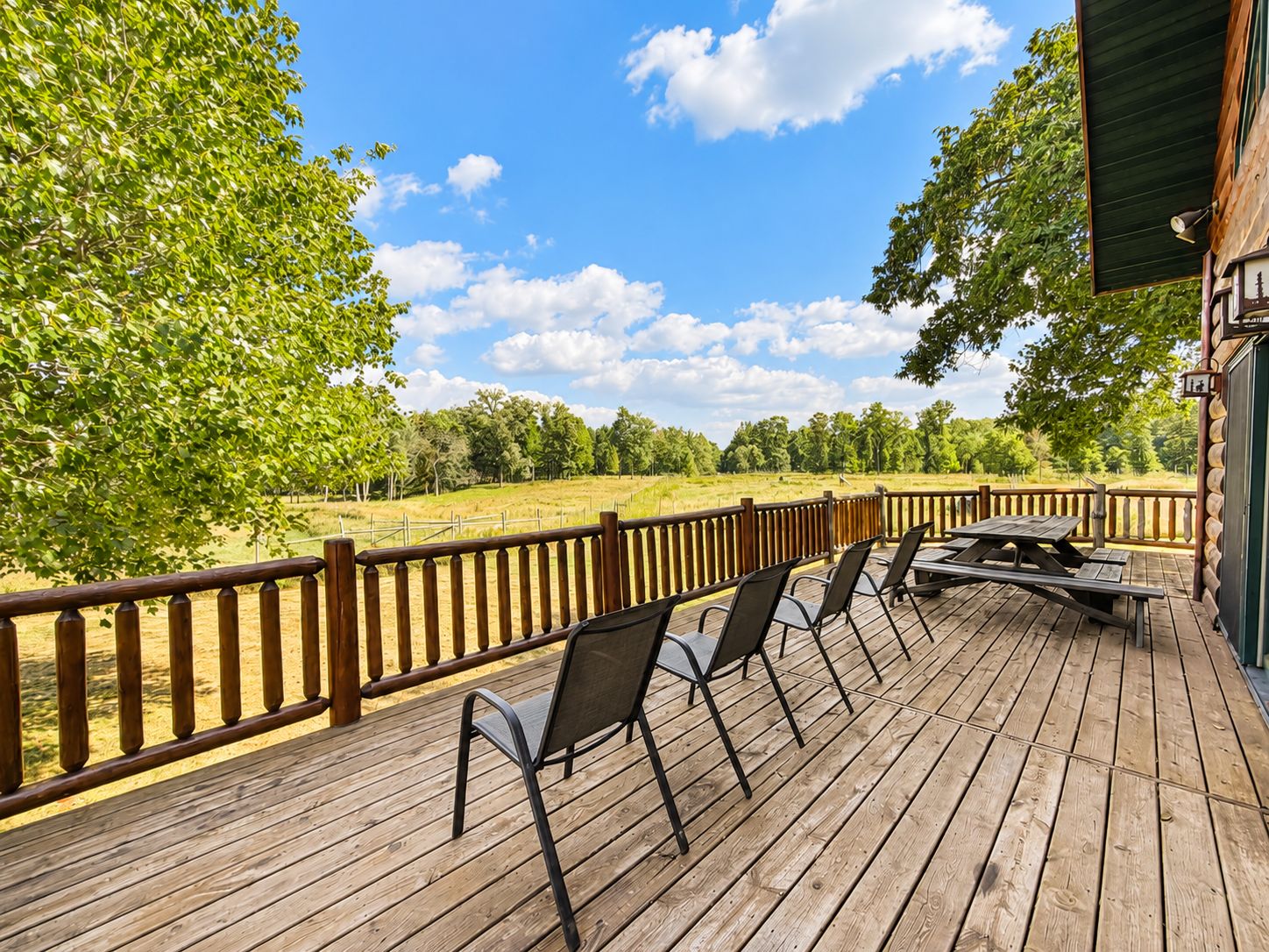 A wooden deck with outdoor seating and a view of a grassy field.