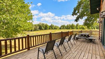 A wooden deck with outdoor seating and a view of a grassy field.