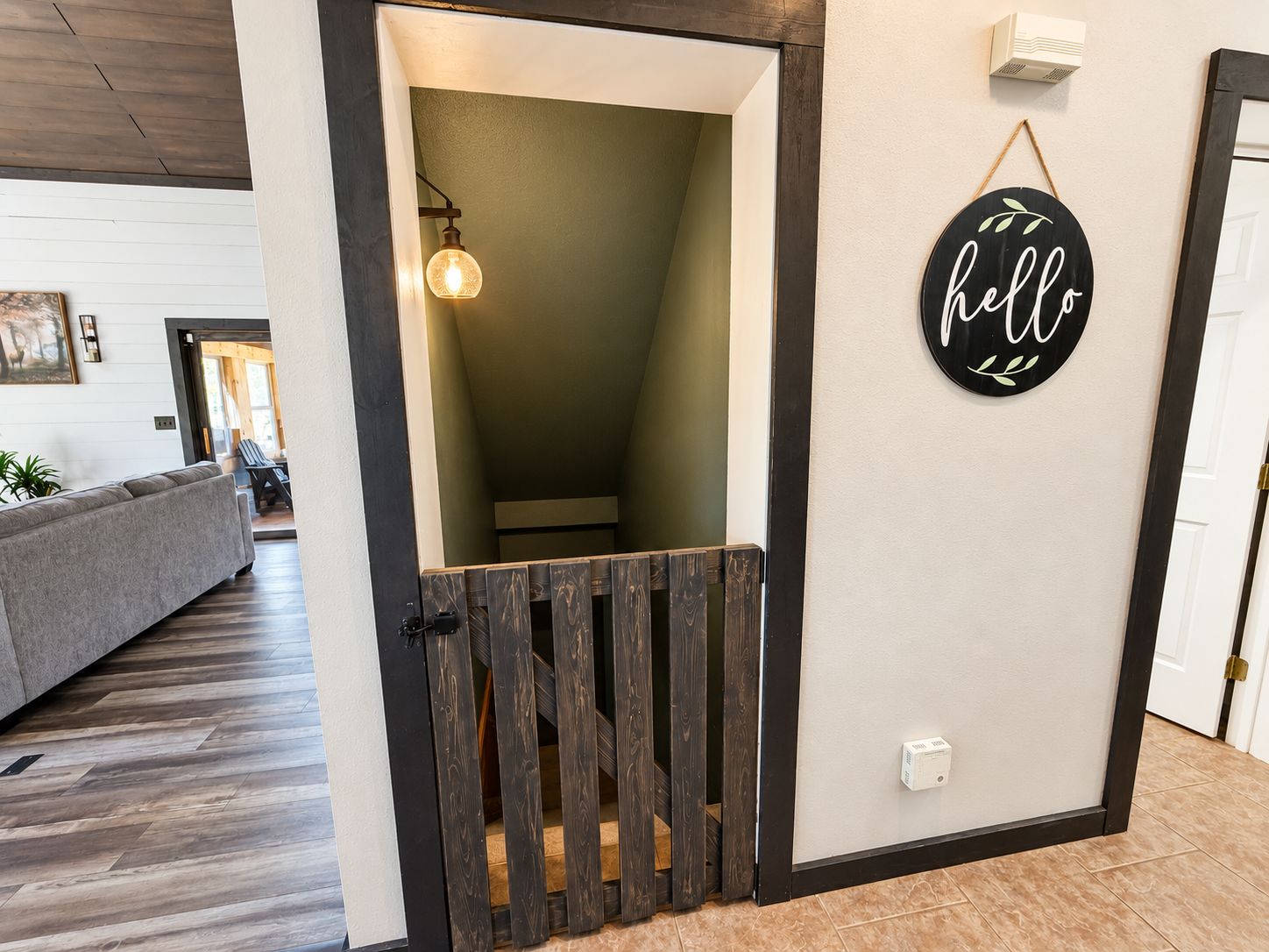 A doorway leading to a stairwell with a wooden gate, a wall-mounted light fixture, and a 'hello' sign.