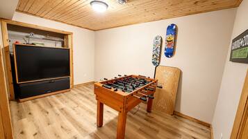 Una habitación con techo de madera, mesa de fútbol de mesa, televisor y zona de juegos.