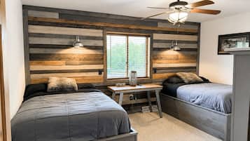 Ein Schlafzimmer mit zwei Betten, einem Schreibtisch, einem Deckenventilator und einem Fenster mit Jalousien.