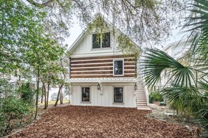 A two-story house with a white exterior and wooden siding, surrounded by trees and a mulched lawn. - Lakeside Villa (Santa Rosa Beach)