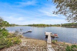 A calm lake with a wooden dock extending into the water, surrounded by trees and vegetation. - Lakeside Villa (Santa Rosa Beach)