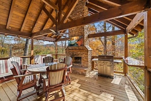 Une terrasse extérieure avec un foyer en pierre, un barbecue et des fauteuils Adirondack.