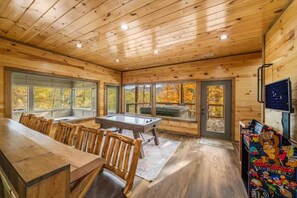 Un intérieur en bois comprenant une table de billard, un coin salon et des jeux d’arcade.
