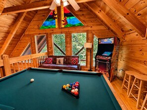 Ein Billardtisch in einer Holzhütte mit einer Couch und einer Flippermaschine.