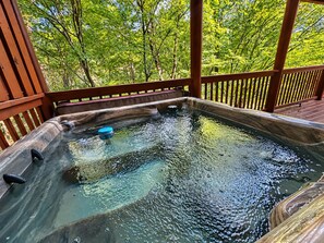 A hot tub on a wooden deck with a view of trees. - 2BR Resort Cabin w/Hot Tub*Game Room*Fireplaces (Pigeon Forge)