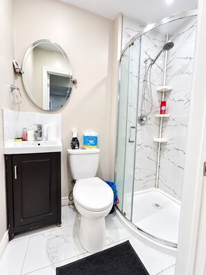 Ein Badezimmer mit Toilette, Waschbecken, Spiegel, Dusche mit Glastür und Wandverkleidung aus Marmorfliesen.