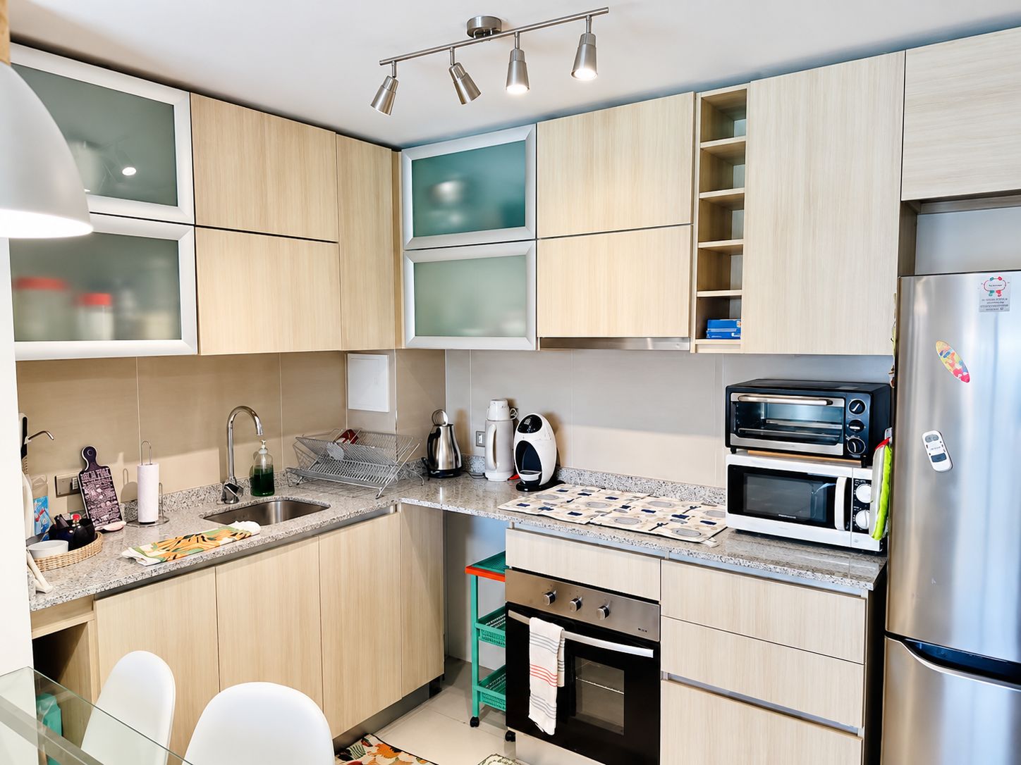 Eine moderne Küche mit Holzausstattung, einem Edelstahlkühlschrank, einer Mikrowelle, einem Toasterofen und einem kleinen Backofen.