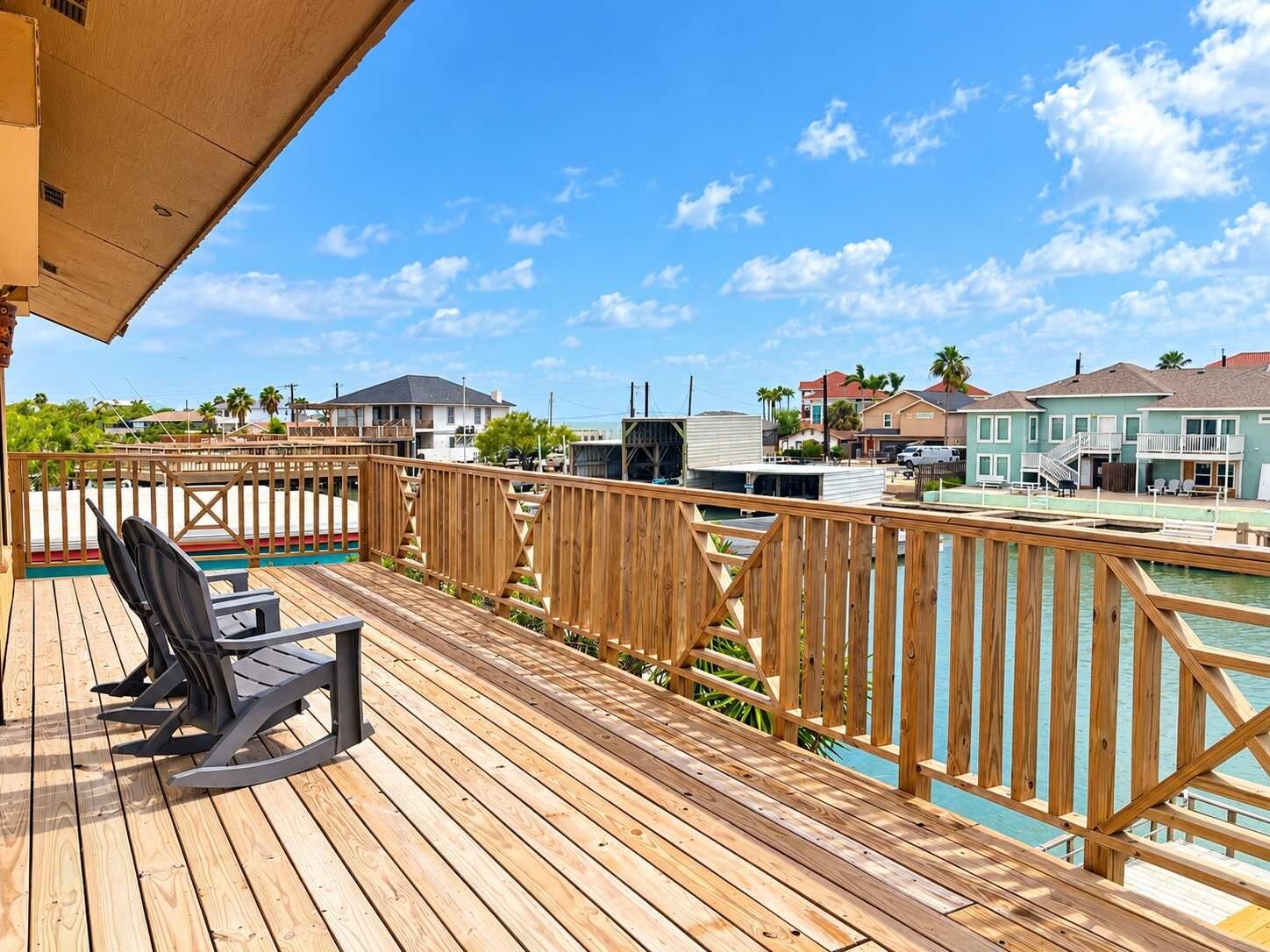 A wooden deck with a pool, overlooking a residential area with houses and a clear sky.