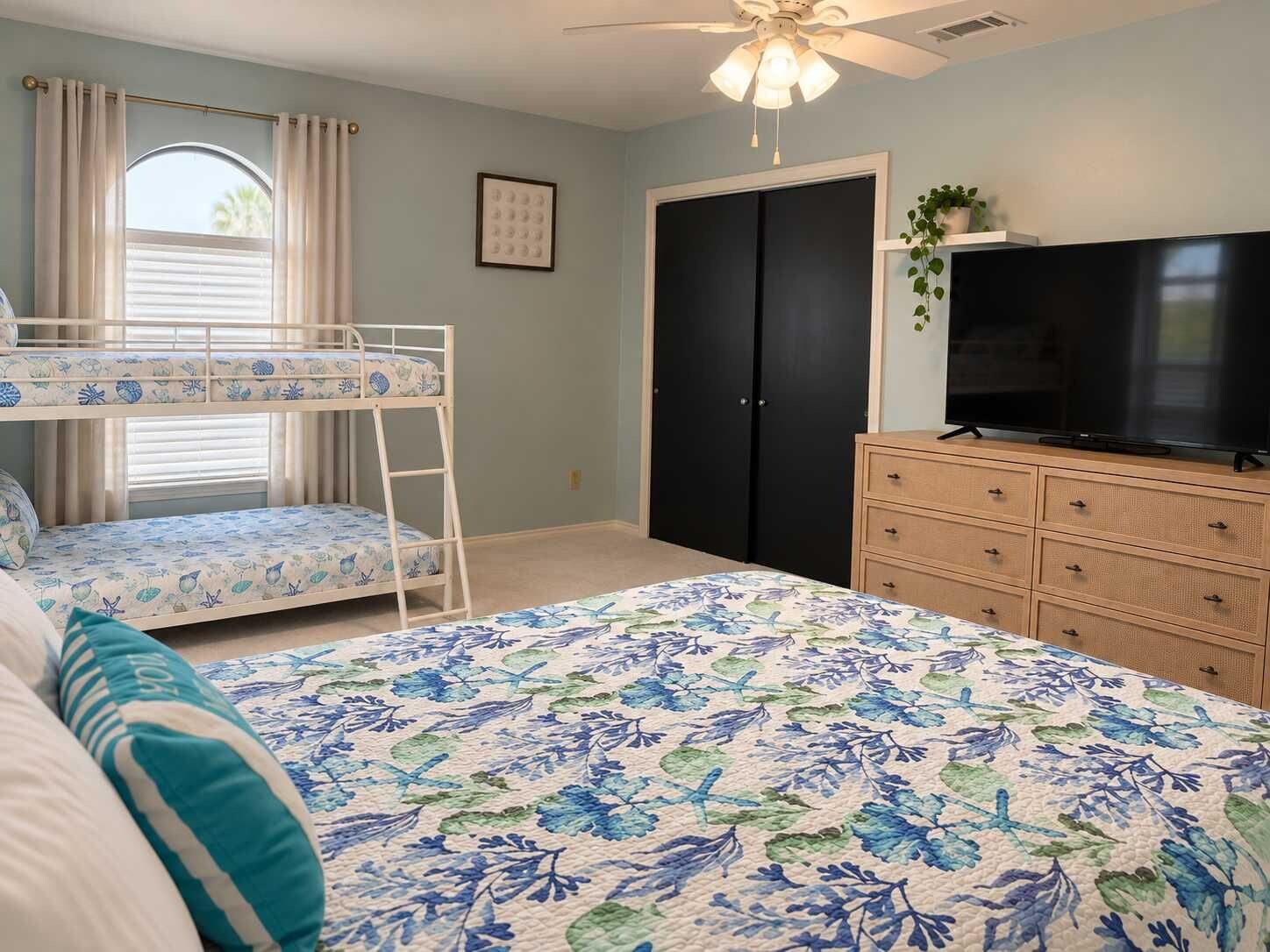 A bedroom with bunk beds, a dresser, a television, and a ceiling fan.