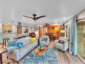 A spacious living area with a sofa, armchairs, and a coffee table. There is a kitchen in the background with a dining area. - Honolii Hale - Oceanfront (Hilo)