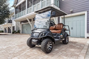 A golf cart parked in front of a residential building with a garage and a covered porch. - The Good Life (Santa Rosa Beach)