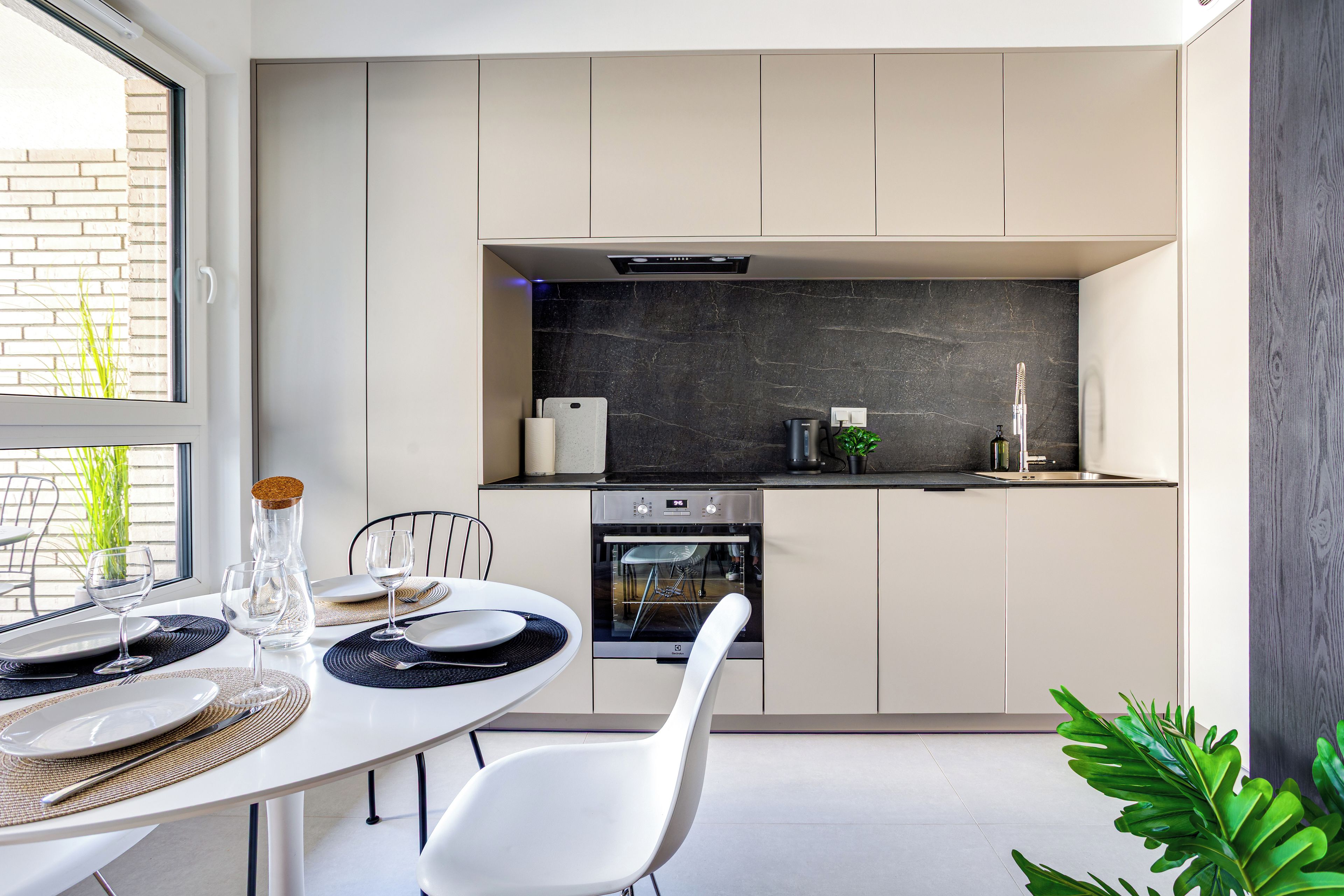 A modern kitchen with a built-in oven, a dining table with chairs, and a view of the outside.