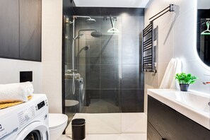 Un bagno moderno con doccia vetrata, lavatrice integrata, un water e un lavandino con una pianta in vaso.