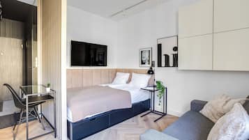 Un dormitorio moderno con cama, escritorio y zona de estar, que incluye un televisor, una obra de arte y una planta.