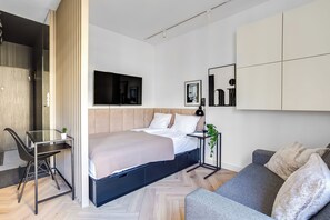 Una camera da letto moderna con un letto, una scrivania e un angolo salotto, con TV, opere d'arte e una pianta.