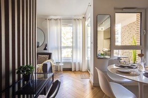 A modern living room with a dining area, a large window with curtains, a potted plant, and a mirror on the wall. - Nowoczesne Studio - Modena (Poznań)
