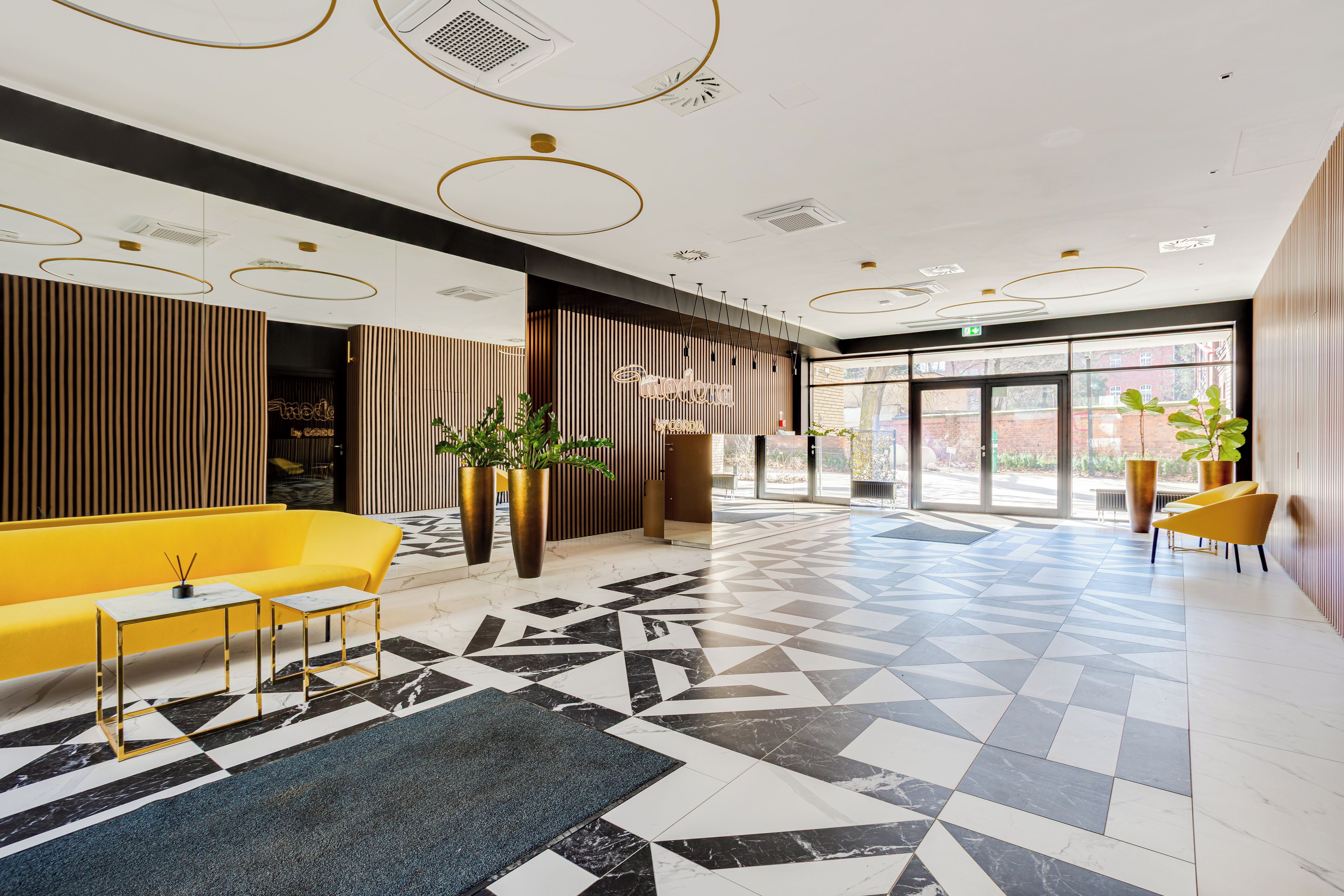 Een moderne lobby met een geruit vloerkleed, een geel zitvlak en een receptiebalie.
