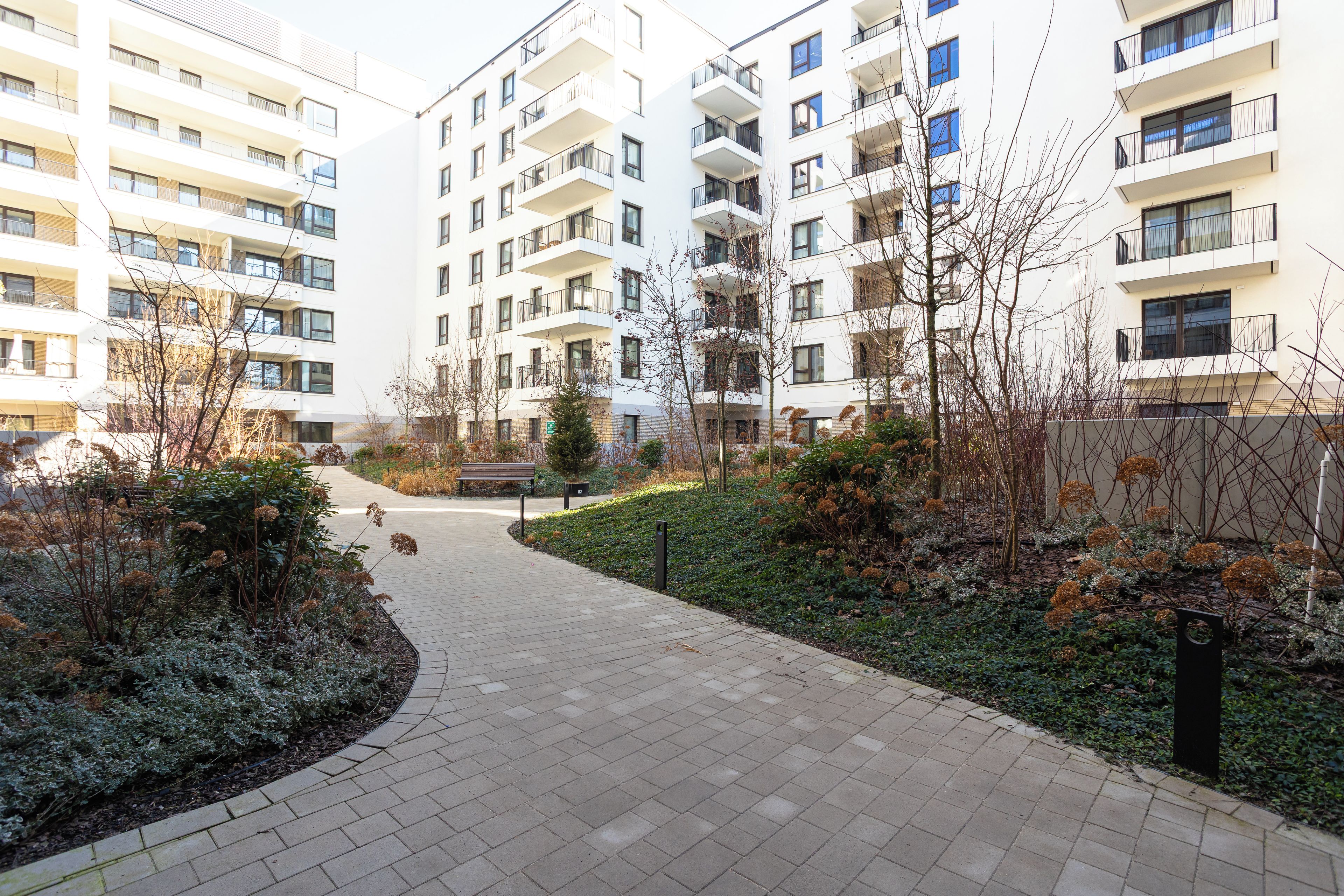 A modern apartment complex with a central courtyard, outdoor seating, and a well-maintained garden area.