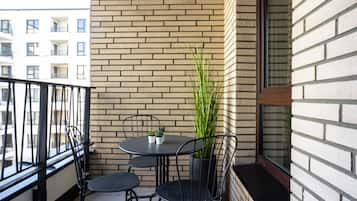 Un balcón con un muro de ladrillo, una mesa redonda con sillas, una planta en maceta y una ventana.