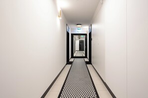 A corridor with a patterned floor, a ceiling light, and a door at the end. - Nowoczesne Studio - Modena (Poznań)