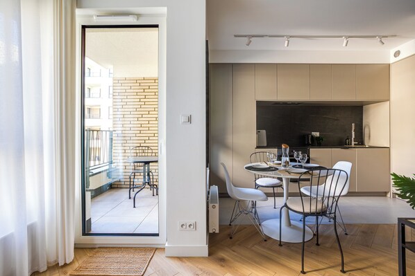 A modern apartment with a balcony, a dining area with white chairs, a kitchen with a black countertop, and a wooden floor. - Nowoczesne Studio - Modena (Poznań)