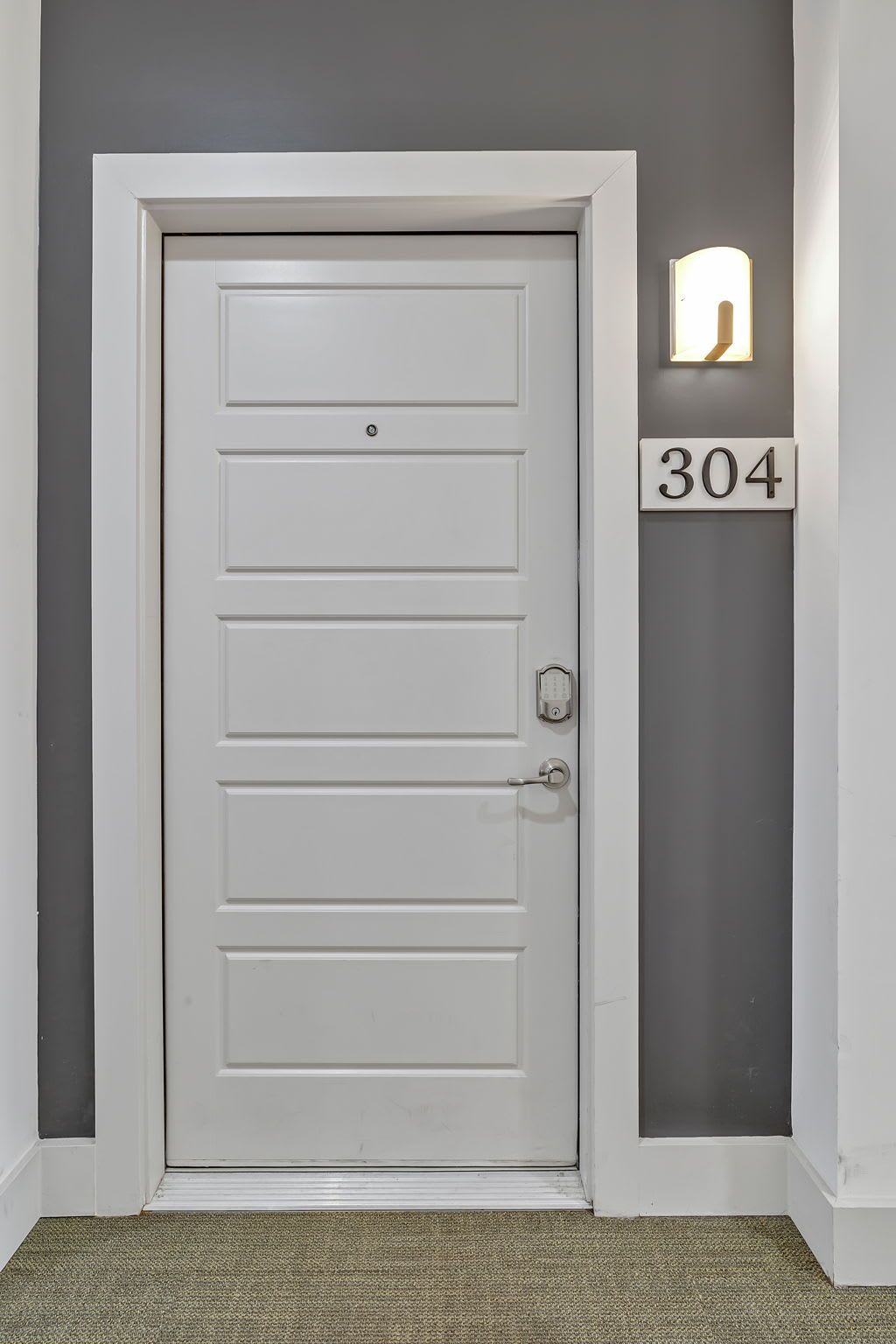En vit dörr med ett kodlås, en ljusströmbrytare och en nummerskylt med siffran ’304’ på väggen bredvid.