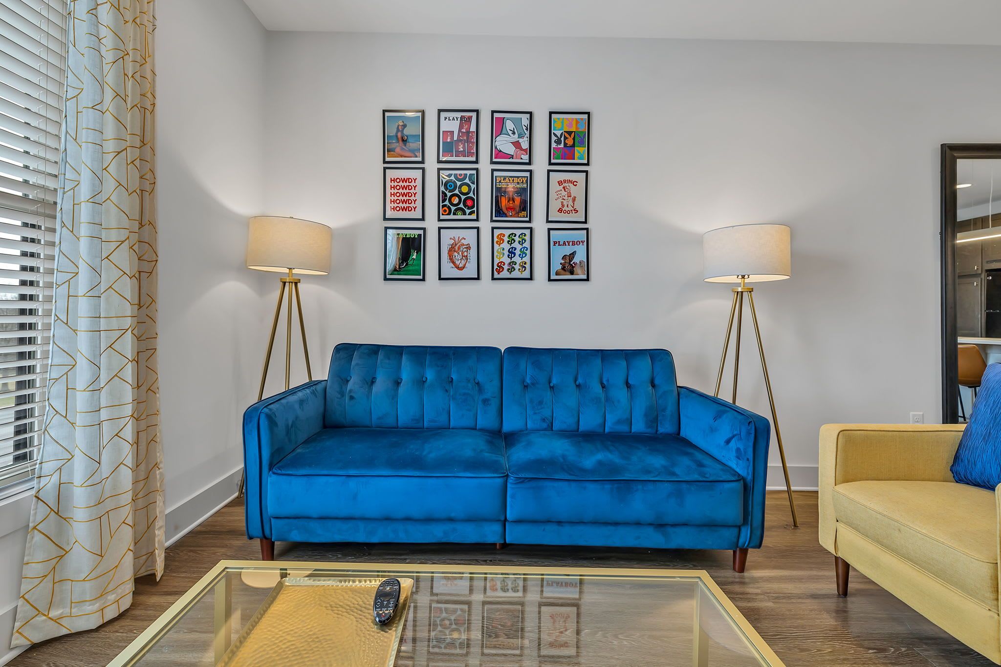 A living room with a blue sofa, a yellow armchair, and a coffee table with a remote control.