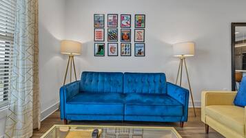 A living room with a blue sofa, a yellow armchair, and a coffee table with a remote control.