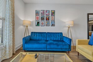 Een woonkamer met een blauwe bank, een gele fauteuil en een salontafel met een afstandsbediening.