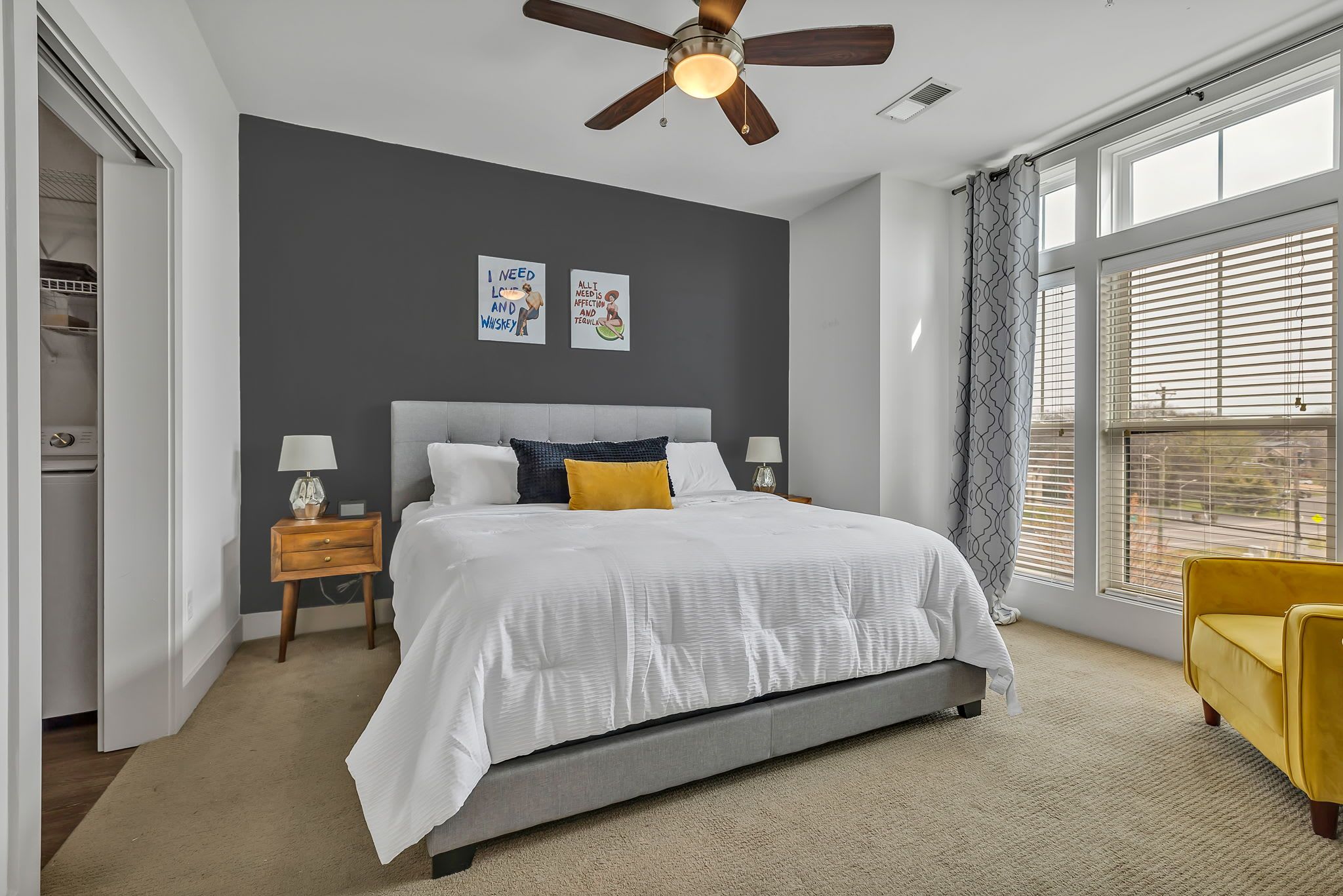 A bedroom with a bed, a ceiling fan, a window with blinds, and a nightstand with a lamp.